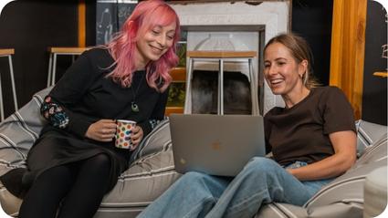 Two young professional women looking at a laptop while sitting on a beanbag Two young professional women looking at a laptop while sitting on a beanbag